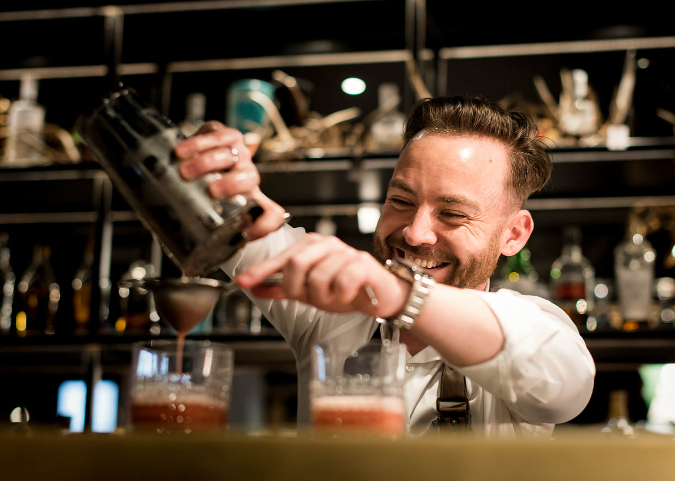 Smiling bartender pours two cocktails from a cocktail shaker