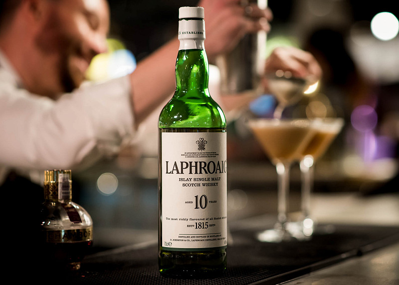 A bartender prepares two cocktails behind a bottle of Laphroaig whisky that is sitting on the bar