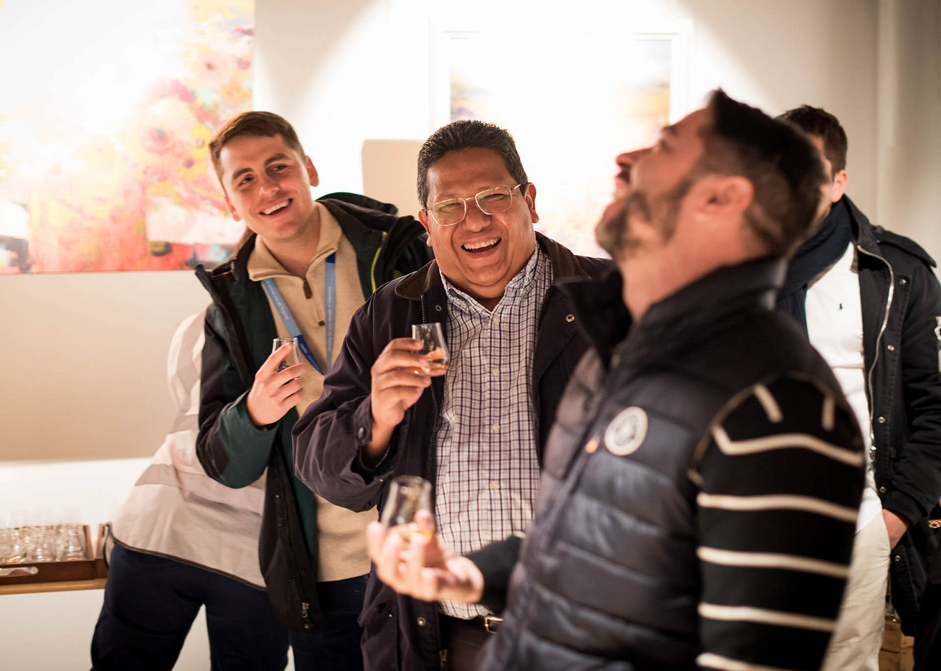 Three men smile and laugh as they sample a whisky at a distillery tour