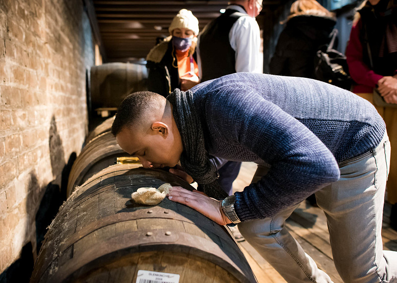 A man leans over a whisky cask to have a smell of it's contents at a distillery