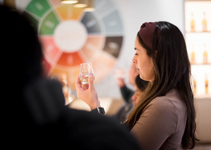 A woman looking at a whisky in a glass during a tasting session at a distillery
