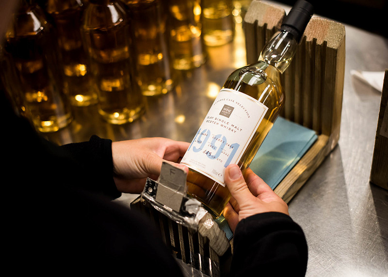 A label is placed onto a recently bottled whisky by hand at a bottling plant