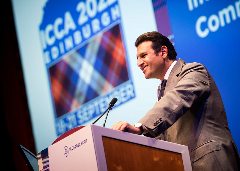 Smiling man with his hand on a lecturn as he speaks at  the ICCA business conference.