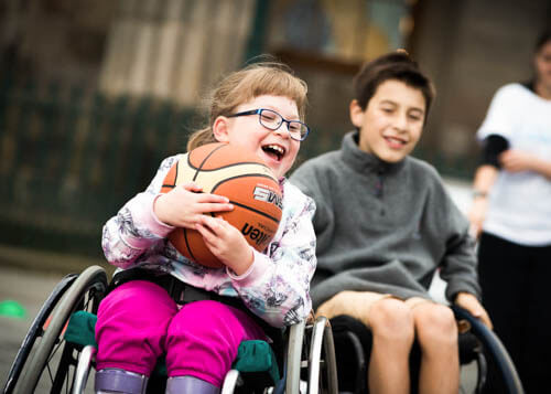 Young girl in wheelchair smiling as she plays basketball