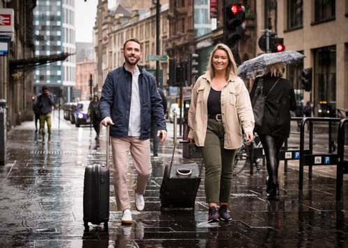 Couple walk along Glasgow street with suitcases